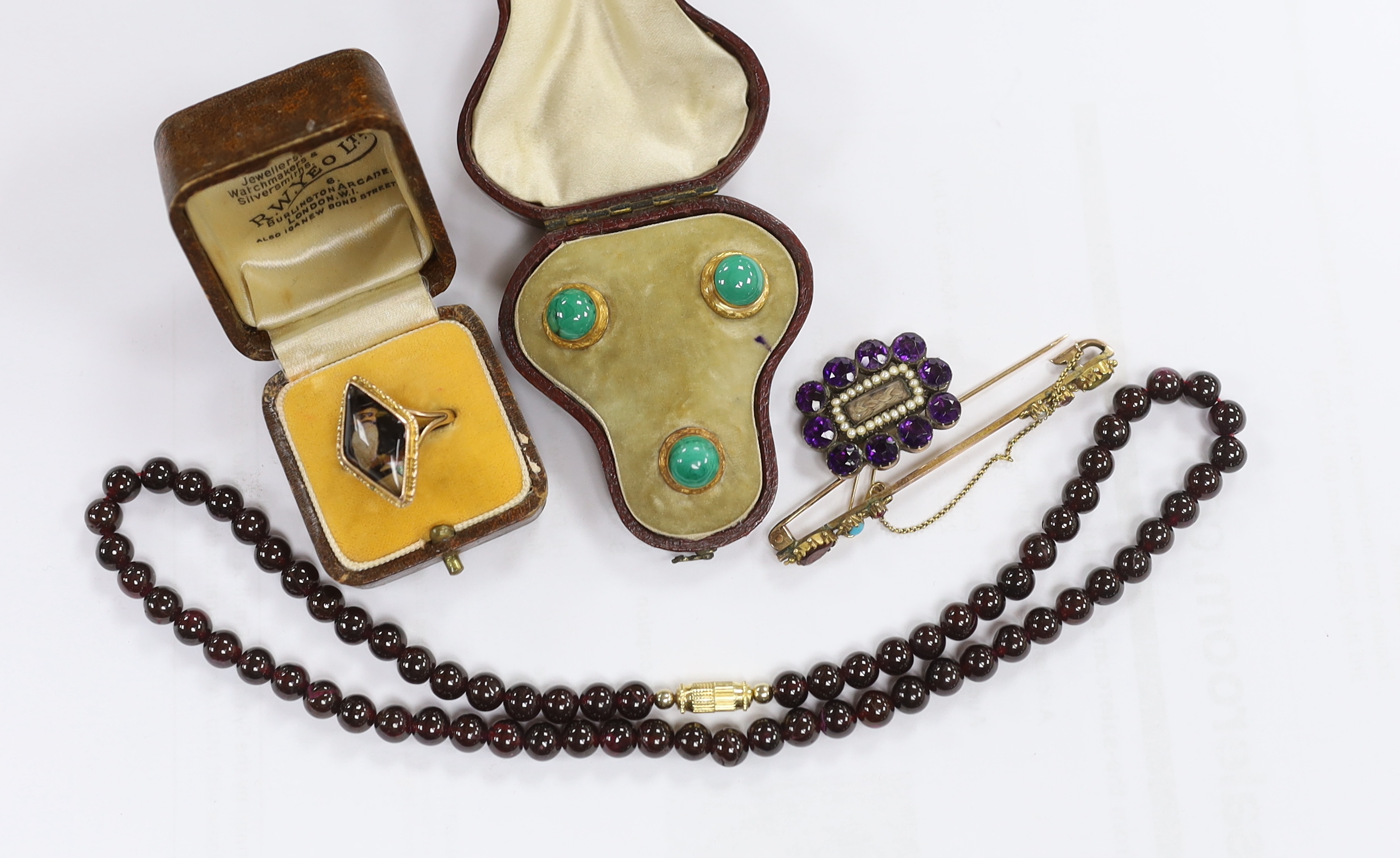 A Georgian amethyst paste and seed pearl set mourning brooch, with plaited hair, 27mm, a cased set of three Edwardian yellow metal and malachite set dress studs, a garnet bead necklace, brooch and a ring.